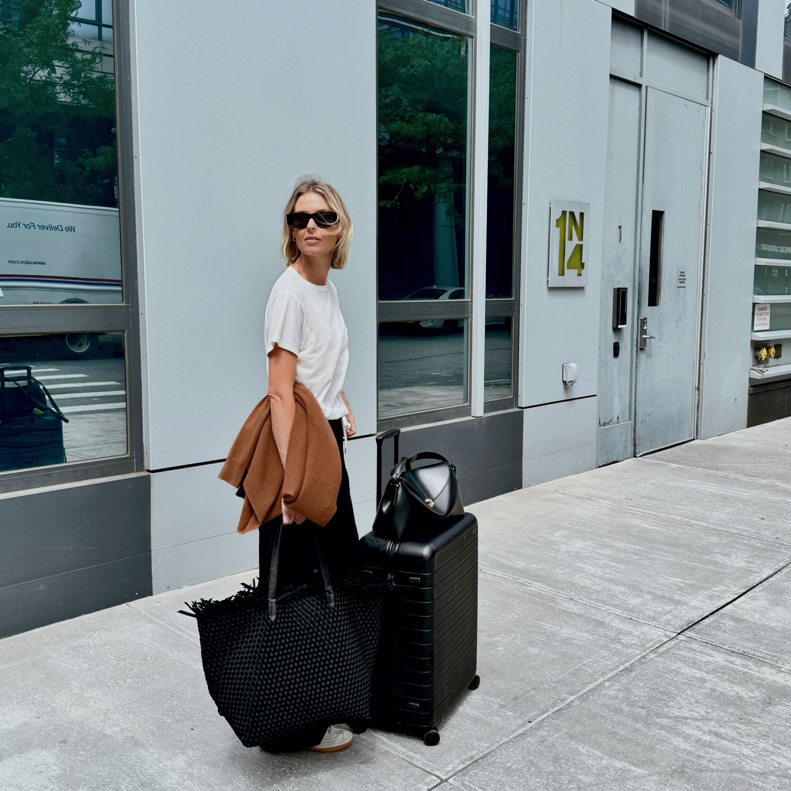 Stylist and fashion editor Natalie Cantell on her way to the airport wearing a neutral travel outfit with Celine sunglasses, Vuori sweatpants, a Nordstrom cashmere sweater, H&M t-shirt, Adidas Sambas, Toteme T-Lock bag, Naghedi oversize tote, and an Away suitcase.