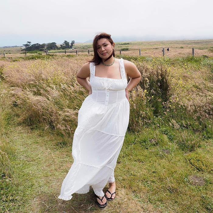 Marina wears white dress and black flip flops while her hair and dress are blown by the wind